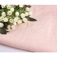 Un bouquet de petites roses blanches avec des feuilles vertes repose sur un morceau plié de Suédine unie embossée au mètre de Longan Craft France, un tissu en daim synthétique de haute qualité parfait pour l'habillement et l'artisanat.