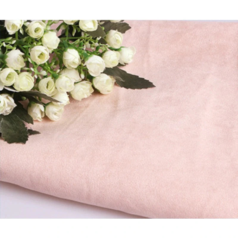 Un bouquet de petites roses blanches avec des feuilles vertes repose sur un morceau plié de Suédine unie embossée au mètre de Longan Craft France, un tissu en daim synthétique de haute qualité parfait pour l'habillement et l'artisanat.
