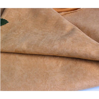 Un gros plan de la Suédine unie embossée au mètre de Longan Craft France montre sa surface brun clair douce et légèrement texturée, pliée et superposée, avec une petite feuille verte dans le coin supérieur gauche.