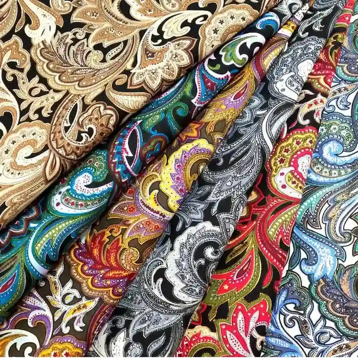 Plusieurs rouleaux de tissu coton imprimé motif paisley ethnique au mètre de Longan Craft France, avec des motifs traditionnels vifs en or, bleu, vert, rouge, noir et blanc, sont disposés côte à côte.