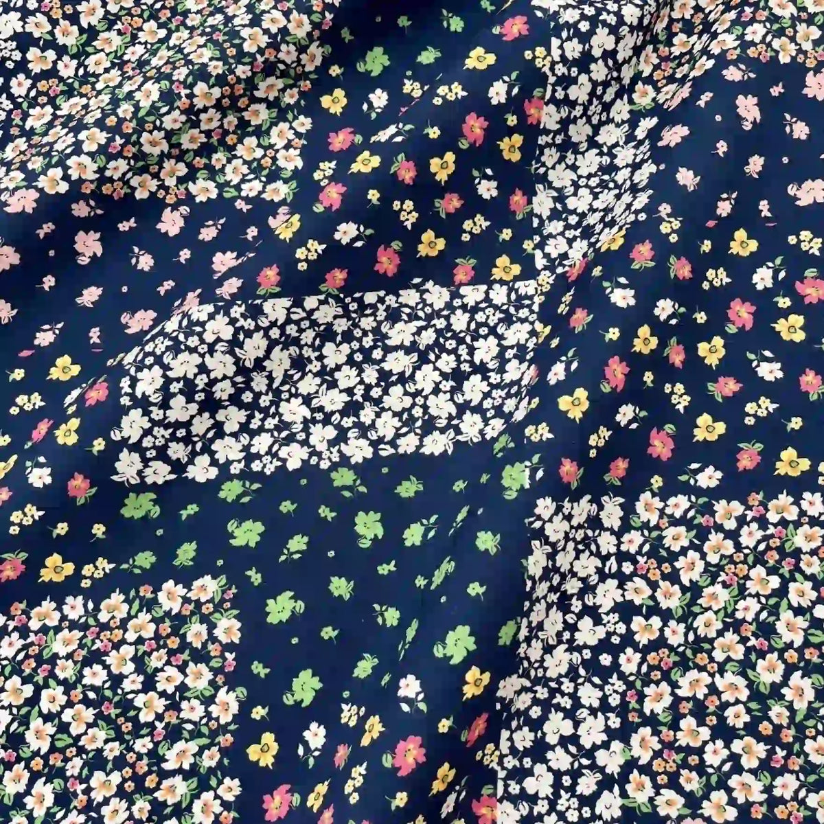 Linon de coton imprimé floral ethnique au mètre par Longan Craft France : tissu linon vintage avec motif patchwork de petites fleurs blanches, jaunes, roses et vertes sur fond bleu foncé, surface légèrement froissée. Idéal pour robes et vêtements.