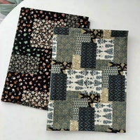 Deux tissus pliés sur une surface blanche : l'un est un Linon de coton imprimé floral ethnique de Longan Craft France sur fond noir, l'autre est un patchwork géométrique dans des tons verts, bleus, beiges et noirs.