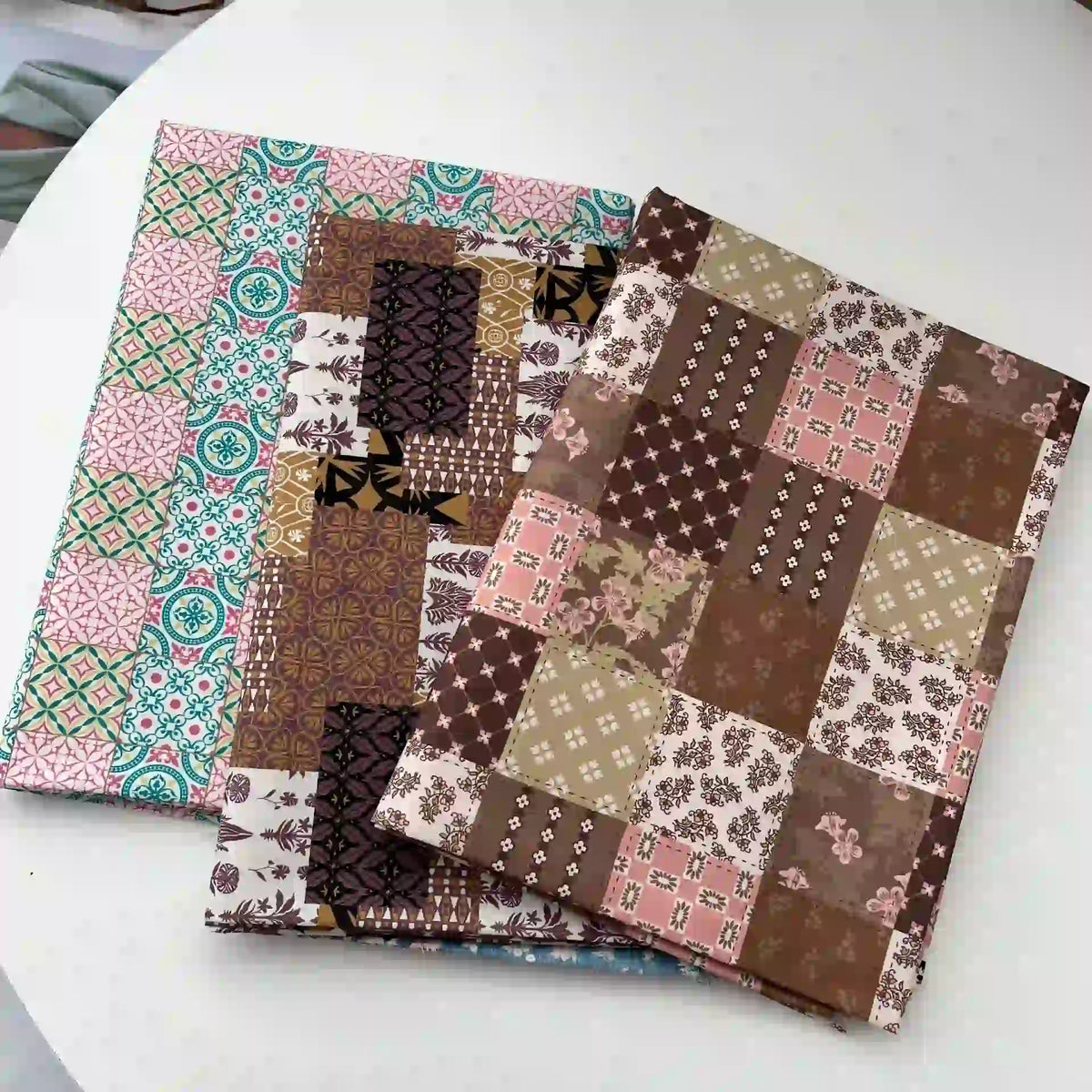 Trois carnets aux couvertures inspirées du Linon de coton imprimé floral ethnique de Longan Craft France, présentant des carrés de patchwork marron et rose ainsi qu'un motif géométrique sarcelle et rose, sont présentés sur une surface blanche.