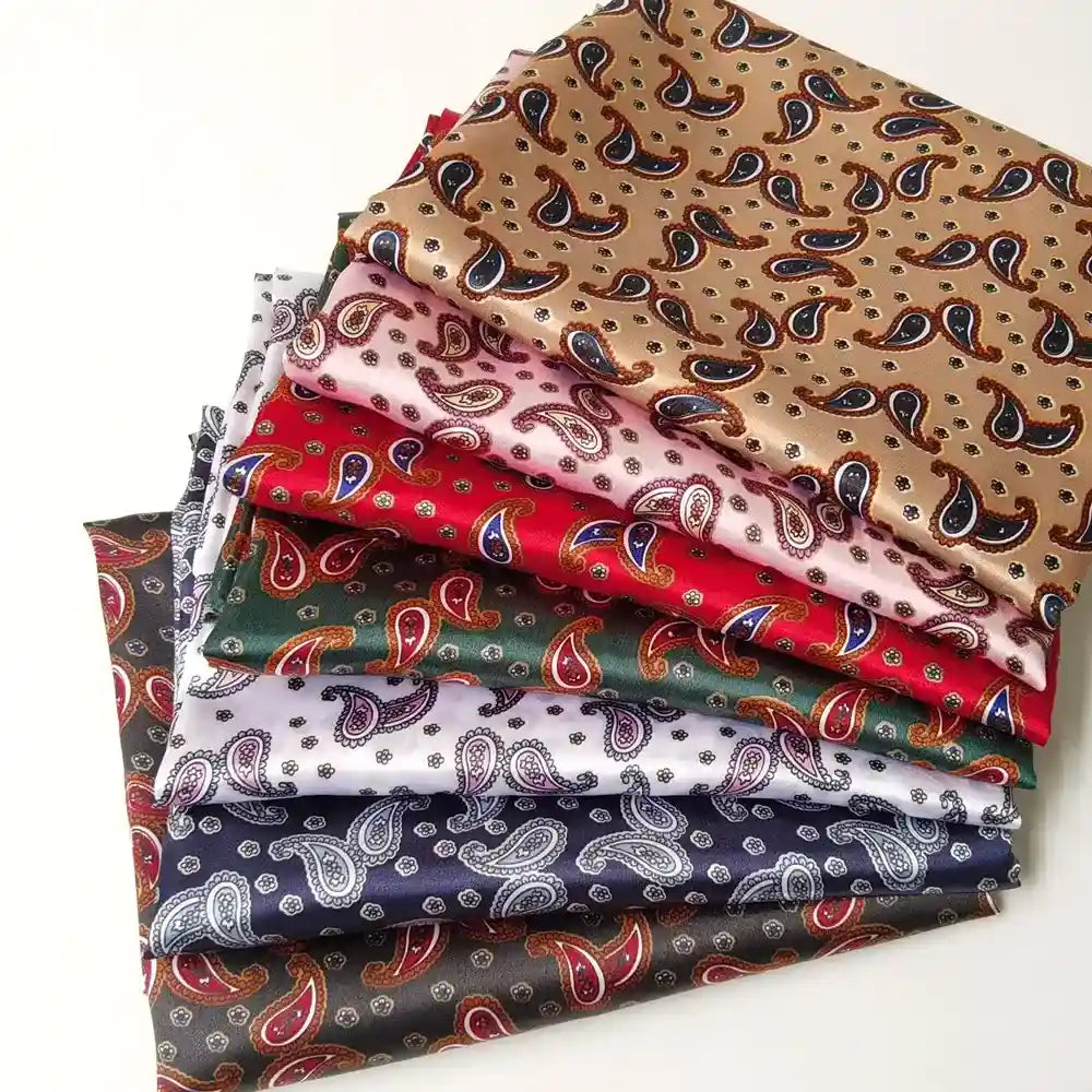 Une pile d'écharpes en satin vibrant, fabriquées à partir du tissu satin polyester imprimé paisley au mètre de Longan Craft France, apporte élégance et couleur grâce à son motif cachemire complexe.