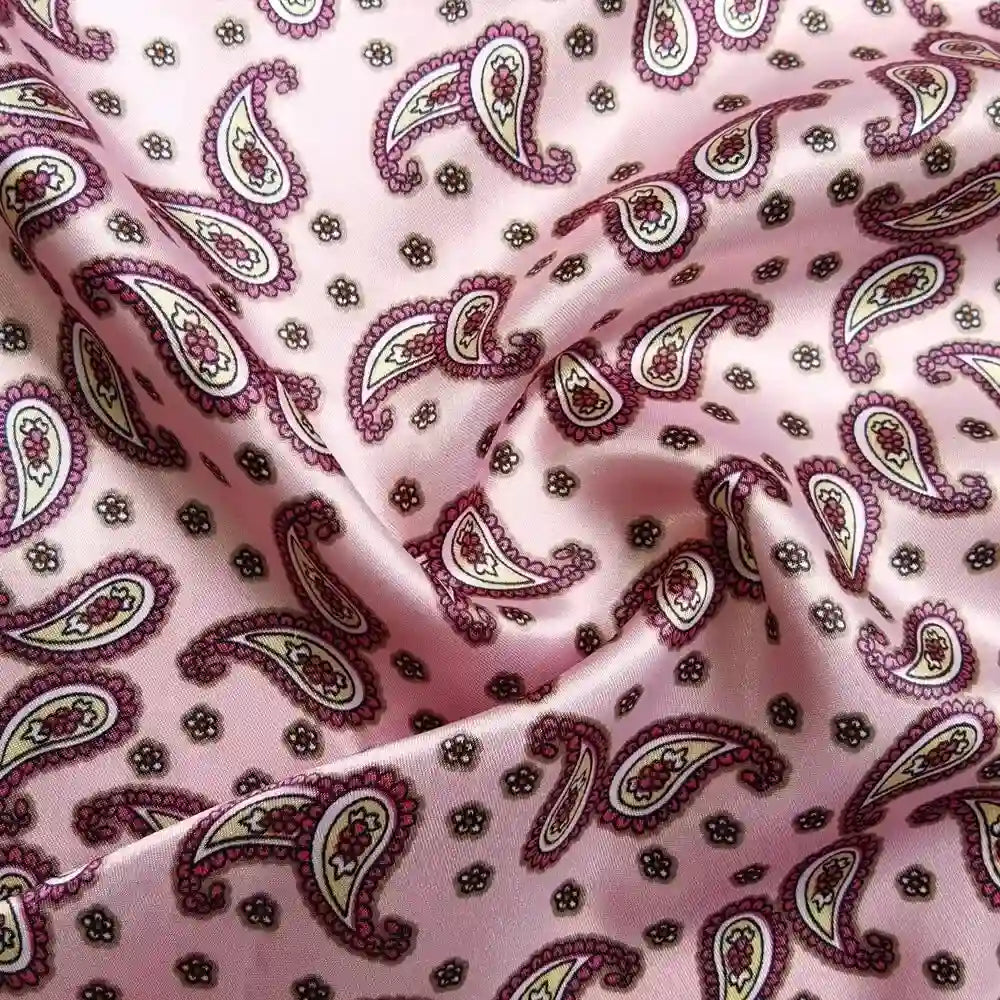 Gros plan sur le Tissu satin polyester imprimé paisley au mètre de Longan Craft France, montrant des motifs colorés de cachemire blanc, marron et jaune avec de petites fleurs. L'élégant tissu de satin est délicatement drapé en plis souples.