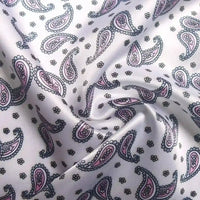 Un gros plan du Tissu satin polyester imprimé paisley de Longan Craft France montre des motifs de cachemire violet pastel et sarcelle avec de petites fleurs noires ; le tissu satin coloré est légèrement froncé, mettant en valeur ses plis élégants et sa texture.