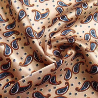 Gros plan sur le Tissu satin polyester imprimé paisley au mètre de Longan Craft France, dont la base est beige et les motifs cachemire marine, orange et blanc. Le satin légèrement froissé crée des plis doux et des ombres élégantes pour des vêtements stylés.