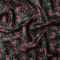 Un gros plan du tissu satin polyester imprimé paisley au mètre de Longan Craft France montre sa couleur vert foncé, son motif paisley rouge et feu, et ses petits motifs, avec le tissu drapé et légèrement froissé.