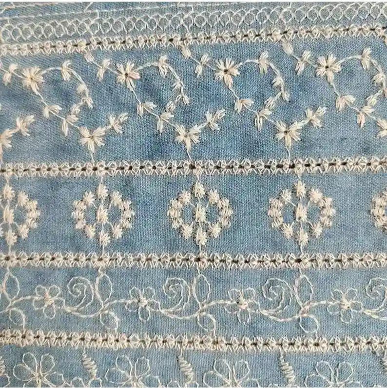 Découvrez le Tissu en coton brodé floral au mètre de Longan Craft France, un tissu en coton ajouré bleu clair avec des broderies florales et géométriques blanches détaillées - un toucher denim idéal pour les robes et les chemisiers.