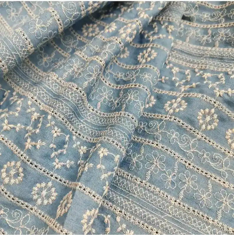 Gros plan sur le "Tissu en coton brodé floral au mètre" bleu clair de Longan Craft France, un tissu denim léger avec des broderies florales ajourées et blanches, parfait pour les robes et les chemisiers.