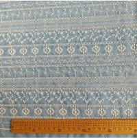 Tissu en coton brodé floral au mètre, bleu clair, de Longan Craft France, présentant des broderies florales et géométriques blanches en rangées horizontales ; une règle en bois située en dessous indique 0-20 cm pour l'échelle. Tissu denim léger idéal pour les robes et les chemisiers.