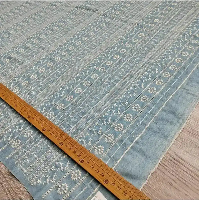 Le Tissu en coton brodé floral au mètre de Longan Craft France, un tissu denim léger avec des broderies blanches complexes, est présenté sur du bois avec une règle marquée en centimètres pour l'échelle. Idéal pour les robes et les chemisiers.