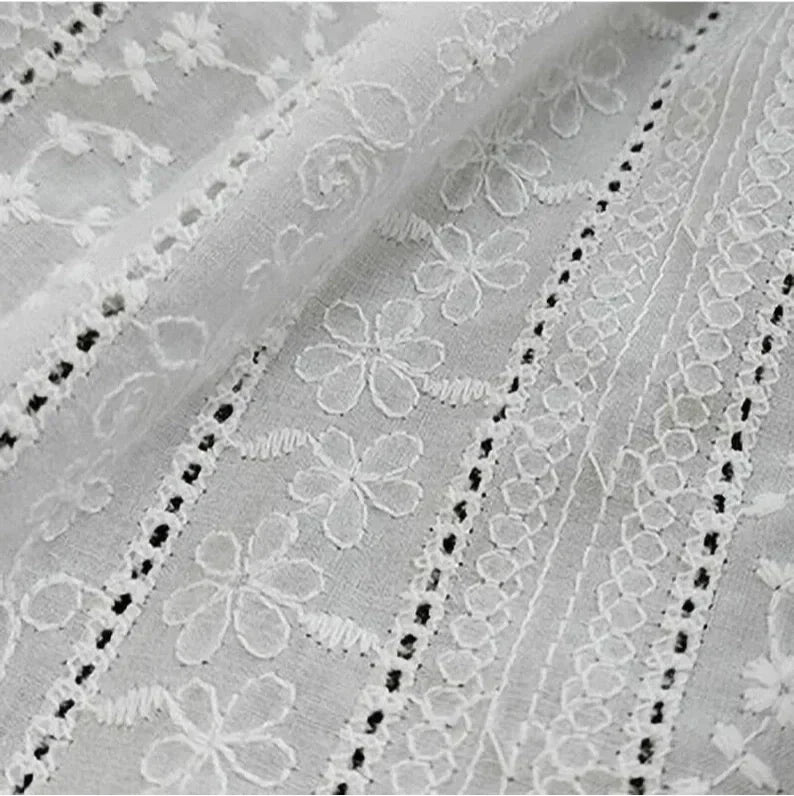 Gros plan sur le Tissu en coton brodé floral au mètre de Longan Craft France : un tissu denim ajouré, léger et semi-transparent, avec des rangées de fleurs et de motifs géométriques brodés, détaillés avec de l'œillet et de la dentelle - idéal pour les robes et les chemisiers.