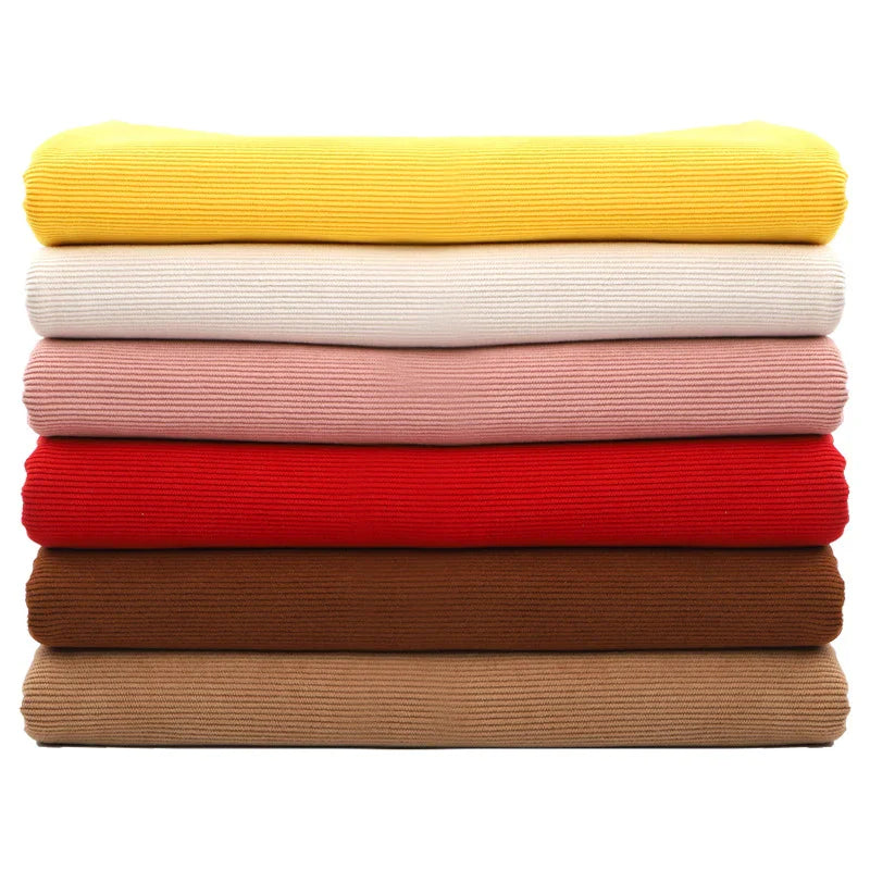 Une pile de six pulls côtelés de couleur jaune, blanc cassé, rose, rouge, marron et beige en Tissu velours côtelé à fines côtes au mètre de Longan Craft France est disposée horizontalement sur un fond blanc.