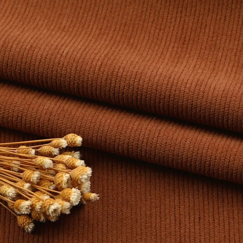 Un gros plan du tissu velours côtelé à fines côtes au mètre de Longan Craft France, avec des fleurs jaunes séchées sur le dessus, met en évidence la texture nervurée et la richesse des couleurs, idéales pour les canapés, les vêtements et les pantalons.