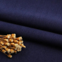 Gros plan sur un pliage en Tissu velours côtelé à fines côtes au mètre de Longan Craft France en bleu foncé avec des fleurs jaunes séchées sur le dessus - parfait pour les projets de tapisserie, de pantalons et de vêtements.