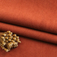 Gros plan sur le Tissu velours côtelé à fines côtes au mètre de Longan Craft France, de couleur rouille, soigneusement plié et surmonté d'un petit paquet de fleurs beiges séchées - idéal pour les canapés, les vêtements ou les pantalons.