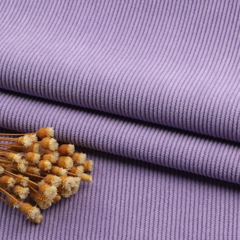 Un morceau de Tissu velours côtelé à fines côtes au mètre de Longan Craft France est plié, sur lequel repose un petit bouquet de fleurs séchées jaunes et blanches.