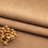 Gros plan sur le tissu velours côtelé à fines côtes au mètre, couleur beige, de Longan Craft France, avec un petit bouquet de fleurs séchées sur le dessus. Idéal pour les canapés, les vêtements et les pantalons.