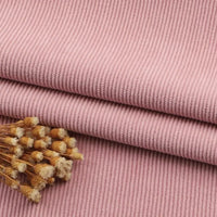 Le tissu velours côtelé à fines côtes au mètre de Longan Craft France est empilé sur une surface, avec des fleurs séchées dans un coin. La texture de ce velours uni, idéal pour les canapés et les vêtements, et les détails des fleurs sont clairement visibles.