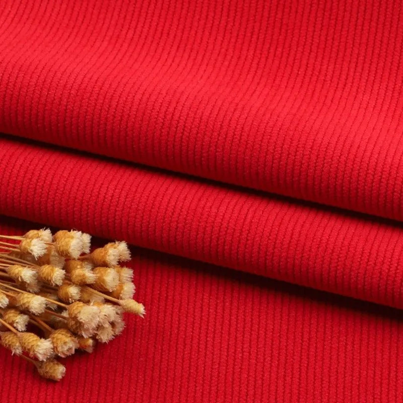 Gros plan sur le tissu velours côtelé à fines côtes au mètre de Longan Craft France, dont la texture et les lignes horizontales sont visibles, avec un petit bouquet de fleurs brunes séchées placé sur le dessus. Idéal pour les canapés, les vêtements et les pantalons.
