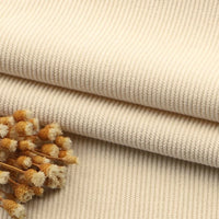 Gros plan sur deux morceaux pliés de Tissu velours côtelé à fines côtes au mètre de Longan Craft France, de couleur beige, avec une petite grappe de fleurs séchées de couleur crème sur le dessus. Idéal pour les canapés, les vêtements ou les pantalons.