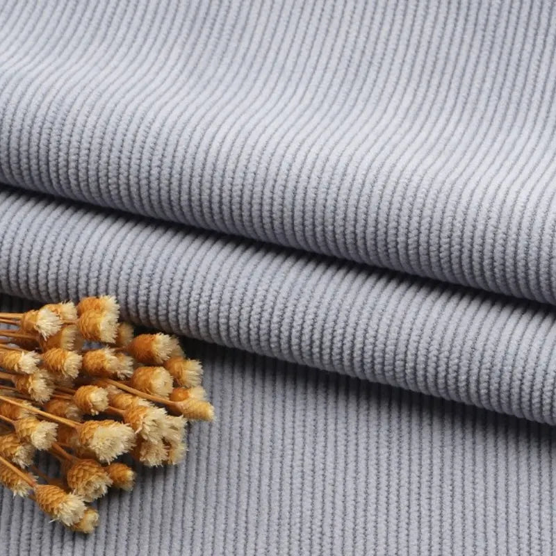 Gros plan sur un pliage en Tissu velours côtelé à fines côtes au mètre de Longan Craft France, en gris clair, avec de petites fleurs séchées jaunes et blanches sur le dessus - parfait pour les canapés, les vêtements ou les pantalons.