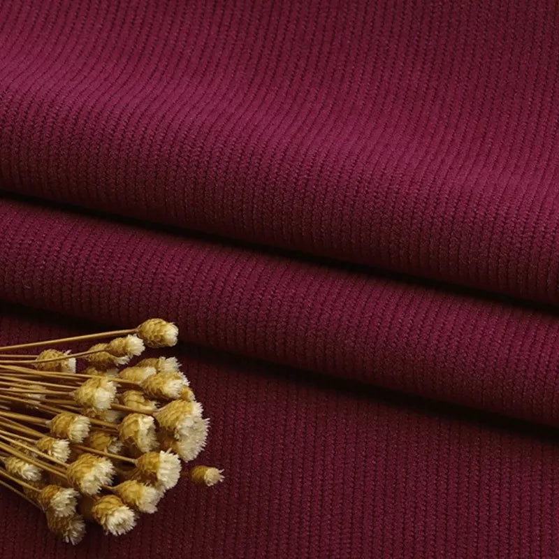Gros plan sur le tissu velours côtelé à fines côtes au mètre de Longan Craft France en marron, soigneusement plié avec des fleurs jaunes séchées sur le dessus, mettant en valeur la texture élégante - idéale pour les canapés, les vêtements et les pantalons.