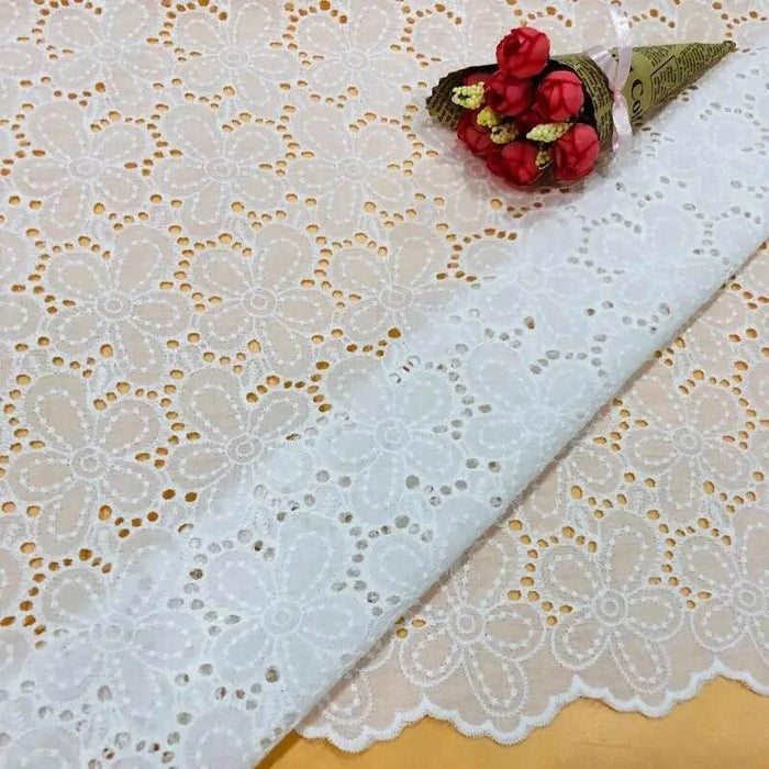 Un morceau de Tissu œillet brodé floral au mètre de Longan Craft France, un tissu floral léger, est posé à plat et recouvert d'un petit bouquet de fleurs artificielles rouges et jaunes enveloppées dans du papier brun.