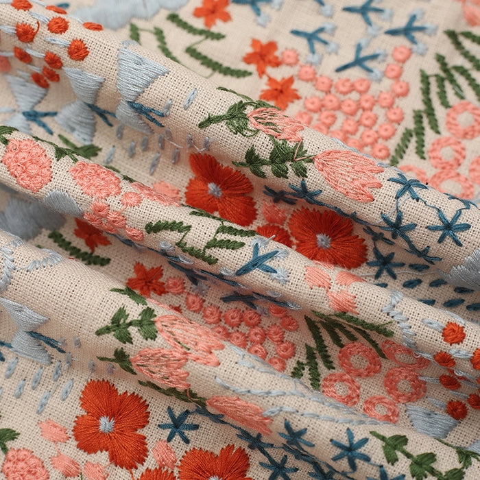 Découvrez le tissu brodé floral au mètre Longan Craft France : coton lin beige orné de fleurs et plantes rouges, roses, bleues et vertes, idéal pour la couture de vêtements ou une décoration intérieure élégante.