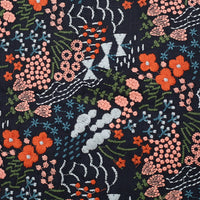 Le tissu brodé floral au mètre, en coton-lin, de Longan Craft France offre un motif de fleurs orange, roses et bleues avec feuilles vertes sur fond sombre et accents géométriques blancs, idéal pour décoration intérieure ou couture.