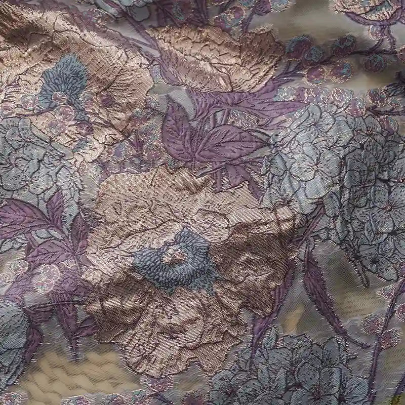 Gros plan sur le Tissu organza brodé floral au mètre de Longan Craft France, un organza transparent avec de grandes fleurs et feuilles de couleur lavande, beige et bleu clair, avec un subtil reflet métallique - idéal pour les robes.