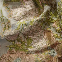 Gros plan sur le Tissu organza brodé floral au mètre de Longan Craft France, un tissu organza transparent pour robes, présentant une broderie florale complexe dans les tons vert, rose, beige et or, avec une texture et des plis visibles.