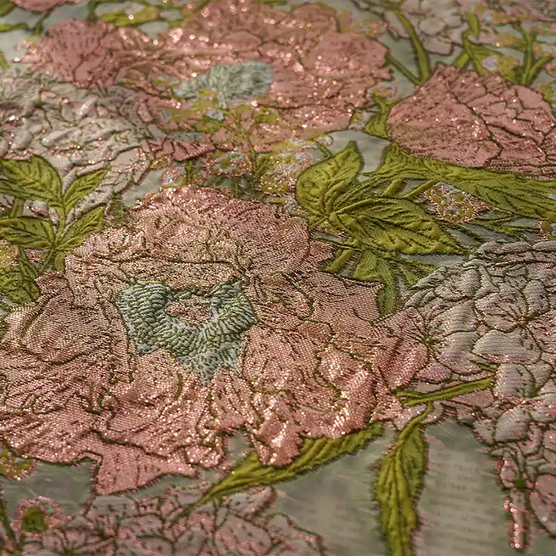 Gros plan sur une broderie florale rose et verte sur Tissu organza brodé floral au mètre par Longan Craft France, montrant de grandes fleurs et feuilles détaillées sur un tissu brillant et transparent idéal pour les robes.