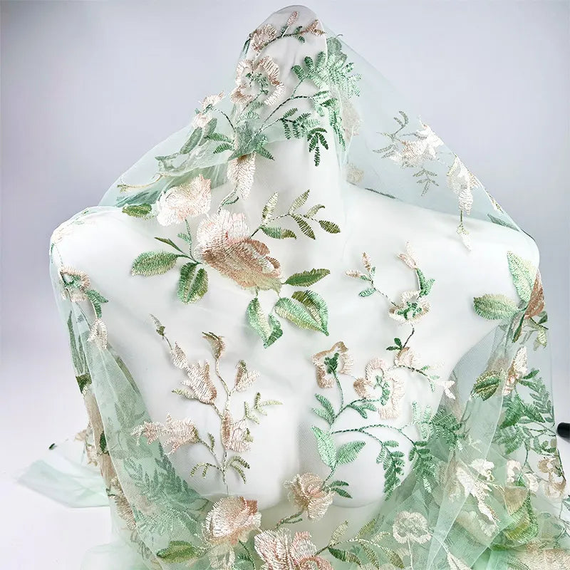 Le Tulle brodé floral au mètre de Longan Craft France, dont les broderies sont vert clair, beige et blanc, est présenté sur un torse de mannequin blanc sur un fond uni. Parfait pour la couture de robes de mariée.