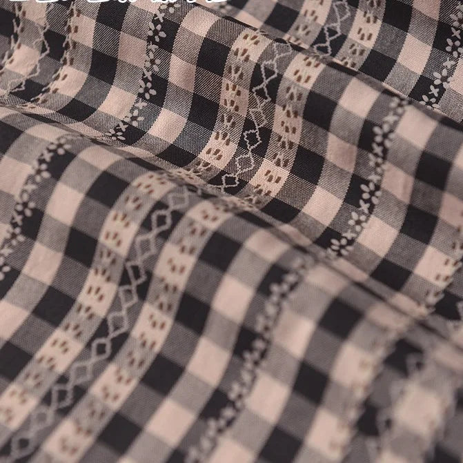 Gros plan sur le Tissu popeline fleurie et vichy au mètre de Longan Craft France, qui présente des broderies décoratives en zigzag et ondulées de couleur beige et blanche sur une popeline douce de coton-polyester noir et blanc, idéale pour les vêtements féminins élégants.