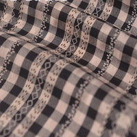 Gros plan sur le Tissu popeline fleurie et vichy au mètre de Longan Craft France, qui présente des broderies décoratives en zigzag et ondulées de couleur beige et blanche sur une popeline douce de coton-polyester noir et blanc, idéale pour les vêtements féminins élégants.