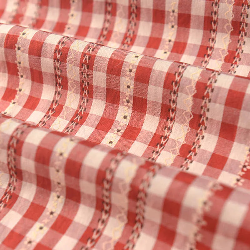 Gros plan sur le Tissu popeline fleurie et vichy au mètre de Longan Craft France, une élégante popeline de coton-polyester à carreaux vichy rouges et blancs, avec des lignes décoratives surpiquées, de petits motifs, des plis doux et une finition subtilement texturée.