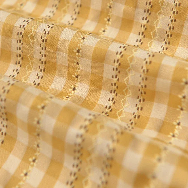 Un gros plan du Tissu popeline fleurie et vichy au mètre de Longan Craft France montre son mélange de coton et de polyester jaune et blanc avec des lignes ondulées brodées et imprimées, des motifs délicats et une finition légèrement froncée, idéale pour les vêtements féminins élégants.