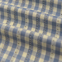 Gros plan sur l'élégant tissu popeline fleurie et vichy au mètre de Longan Craft France, à carreaux bleus et blancs avec surpiqûres décoratives, en coton polyester - parfait pour des vêtements féminins élégants.