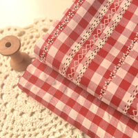Tissu popeline fleurie et vichy de Longan Craft France est plié sur une napperon crocheté, avec une bobine en bois posée à gauche. Popeline élégante en coton et polyester pour vêtements féminins.