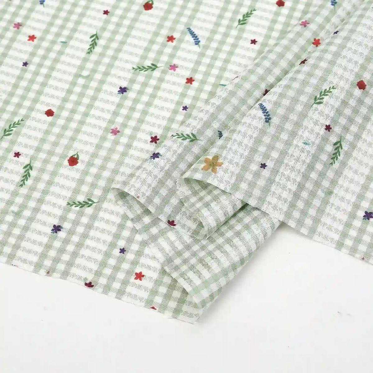 Gros plan sur le tissu pour patchwork vichy au mètre de Longan Craft France, un tissu polyester botanique vert clair et blanc, légèrement plié pour révéler l'endroit et l'envers, idéal pour vêtements décontractés et projets créatifs.