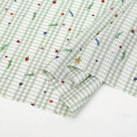 Gros plan sur le tissu pour patchwork vichy au mètre de Longan Craft France, un tissu polyester botanique vert clair et blanc, légèrement plié pour révéler l'endroit et l'envers, idéal pour vêtements décontractés et projets créatifs.