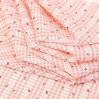 Gros plan sur le tissu pour patchwork vichy au mètre de Longan Craft France, un tissu polyester confortable aux motifs botaniques roses et blancs - parfait pour les vêtements décontractés - délicatement plié en couches superposées.
