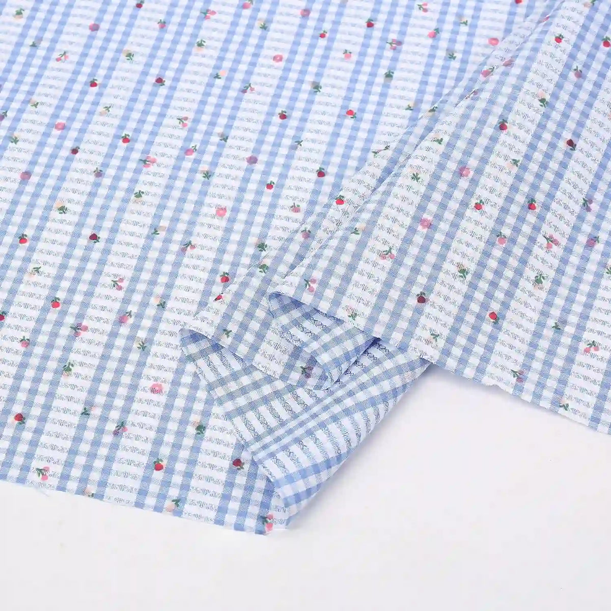 Un morceau du Tissu pour patchwork vichy au mètre de Longan Craft France, un tissu polyester confortable avec des motifs botaniques, est partiellement plié sur une surface blanche. Idéal pour les vêtements décontractés et les projets de patchwork.