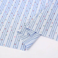 Un morceau du Tissu pour patchwork vichy au mètre de Longan Craft France, un tissu polyester confortable avec des motifs botaniques, est partiellement plié sur une surface blanche. Idéal pour les vêtements décontractés et les projets de patchwork.