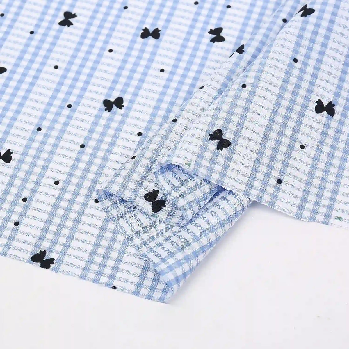 A light blue and white Longan Craft France tissu pour patchwork vichy au mètre, en polyester à motif botanique, partiellement plié pour révéler son motif charmant et sa texture confortable idéale pour vêtements décontractés.