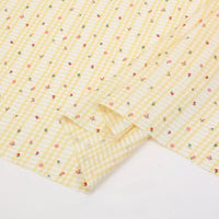 Le tissu Longan Craft France pour patchwork vichy au mètre est un tissu polyester jaune clair à motif botanique, orné de carreaux blancs et de petites fleurs rouges, roses et vertes, idéal pour vêtements décontractés.
