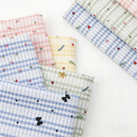 Plusieurs pièces du tissu patchwork vichy au mètre en polyester de Longan Craft France sont disposées sur une surface blanche, mettant en valeur de confortables motifs à carreaux pastel avec des motifs botaniques et floraux, idéaux pour les vêtements décontractés.