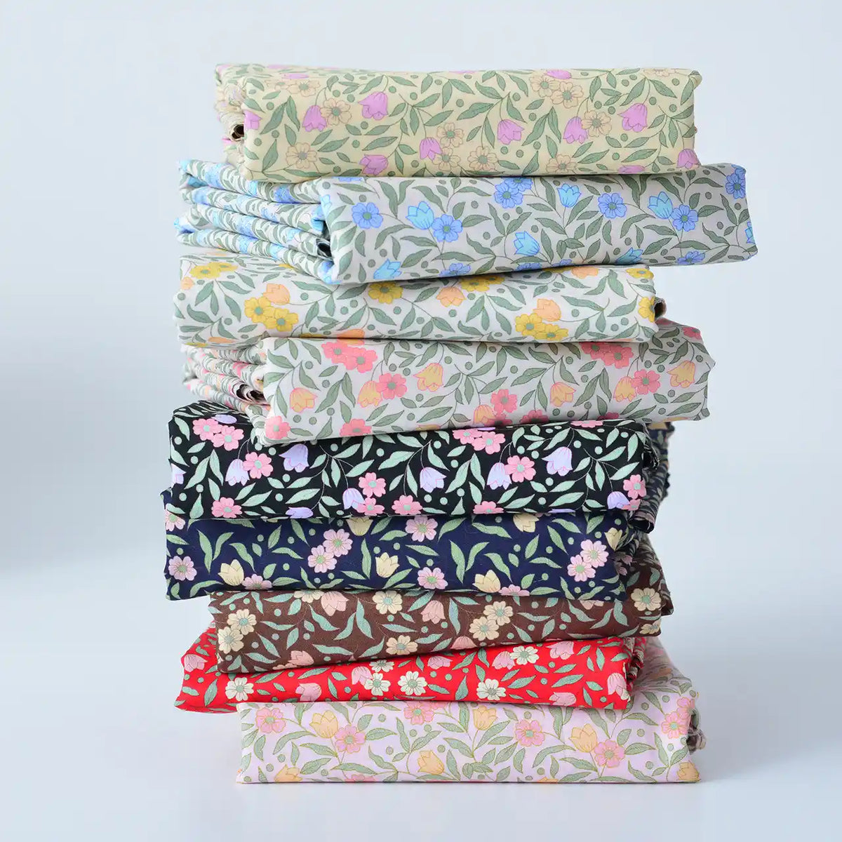 Une pile de tissus colorés en linon et voile de coton imprimé de Longan Craft France, parfaits pour les vêtements et les doublures, disposés sur un fond clair uni.